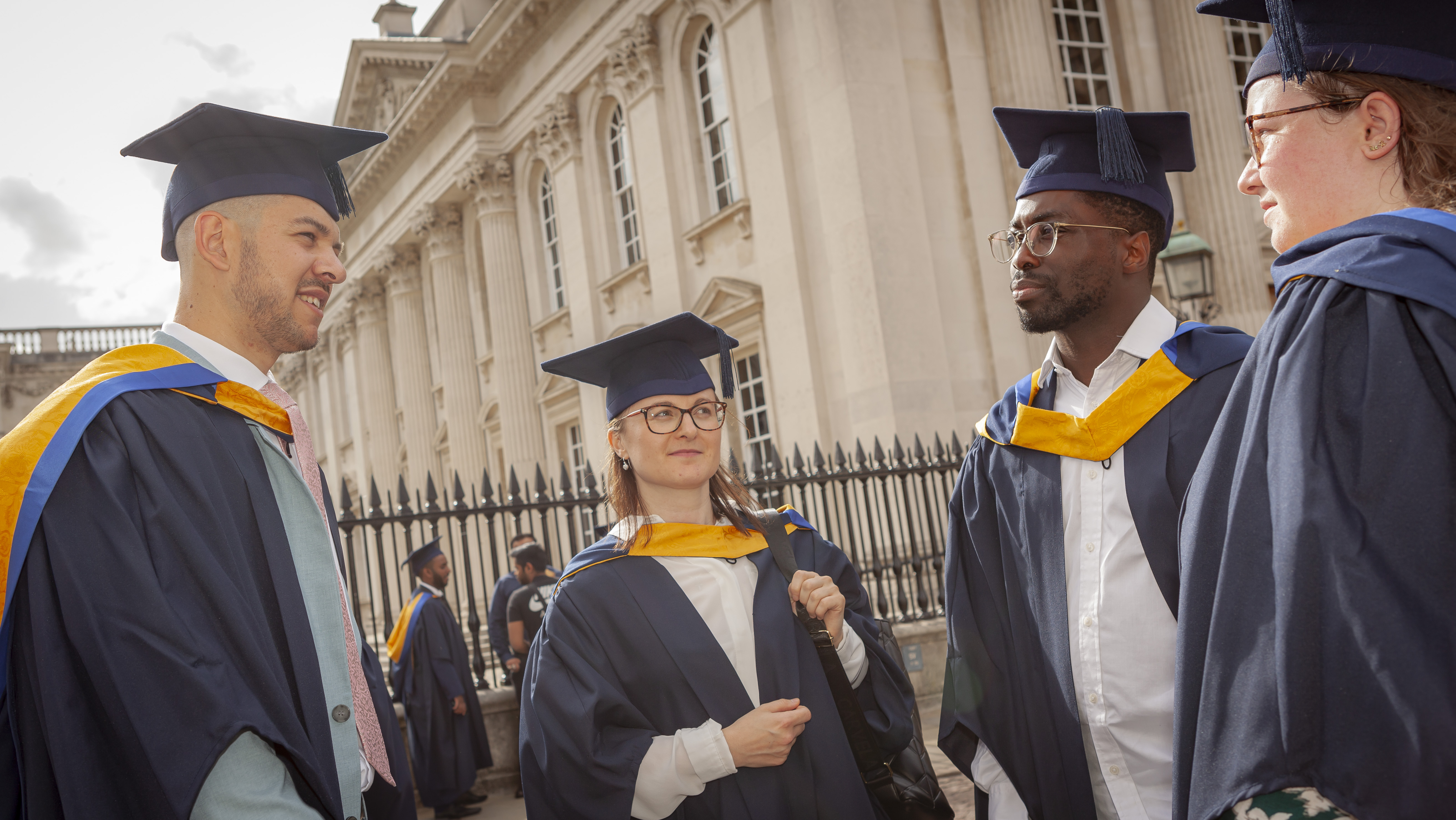 Several of Cambridge's cohort of data scientist apprentice graduates talk to each other dressed in navy and yellow cap and gowns