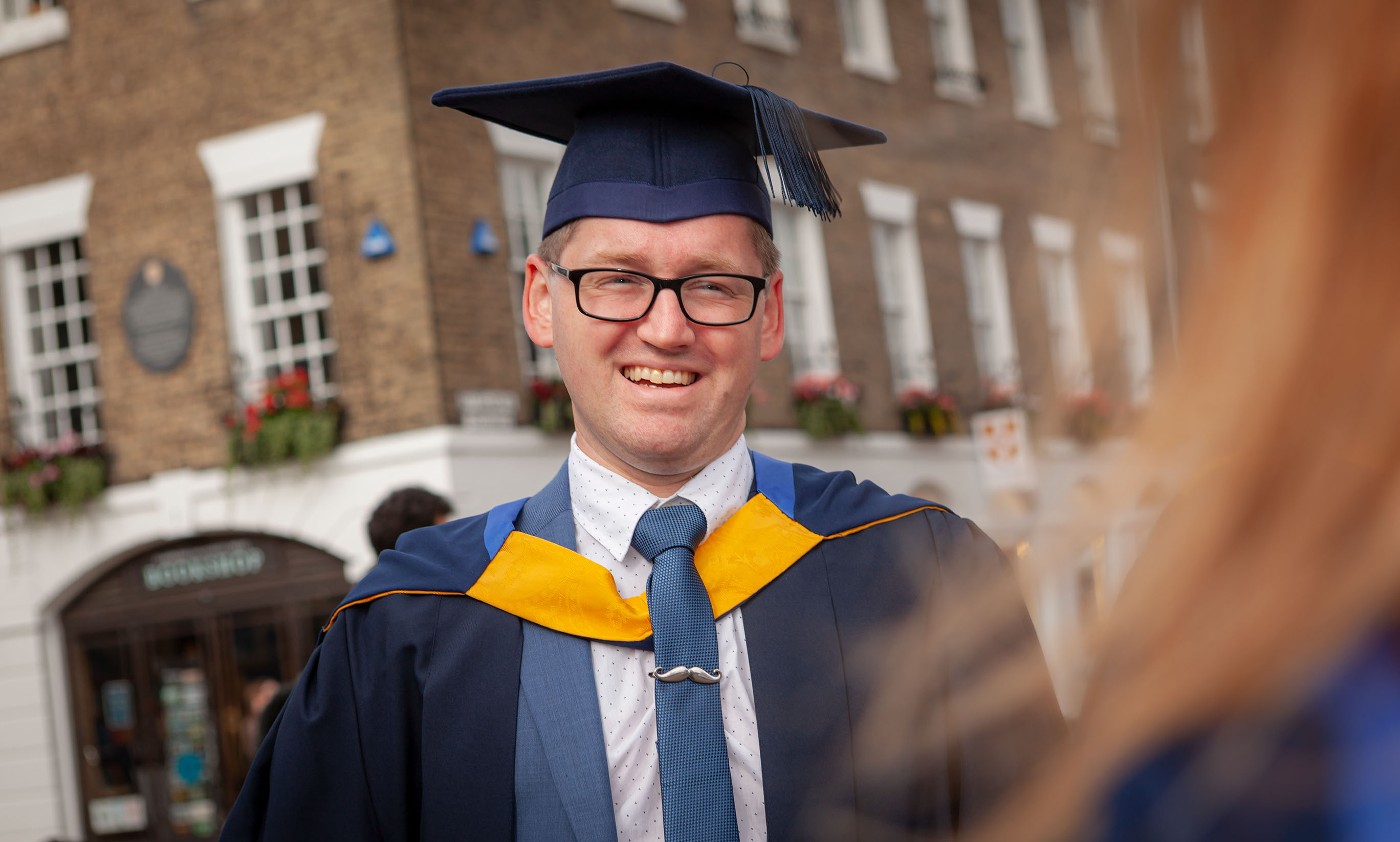 Data scientist apprentice graduate, Pat Robbie dressed in navy and yellow cap & gown.